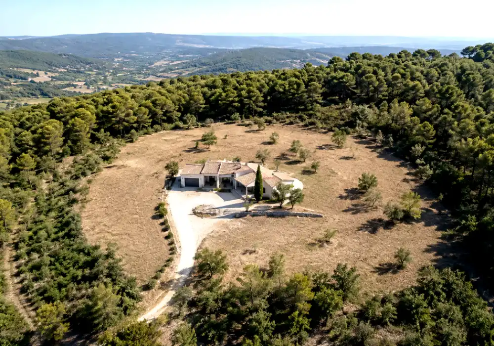 Personne travaillant à la débroussailleuse dans un jardin avec végétation dense près d’une habitation.